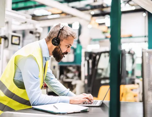 An engineer with a headset working on a laptop on the factory floor